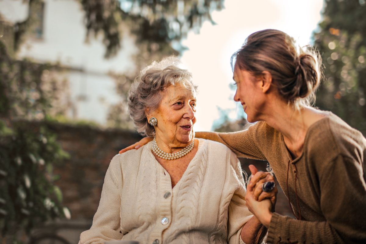 An older woman and a younger woman holding hands and talking warmly outdoors